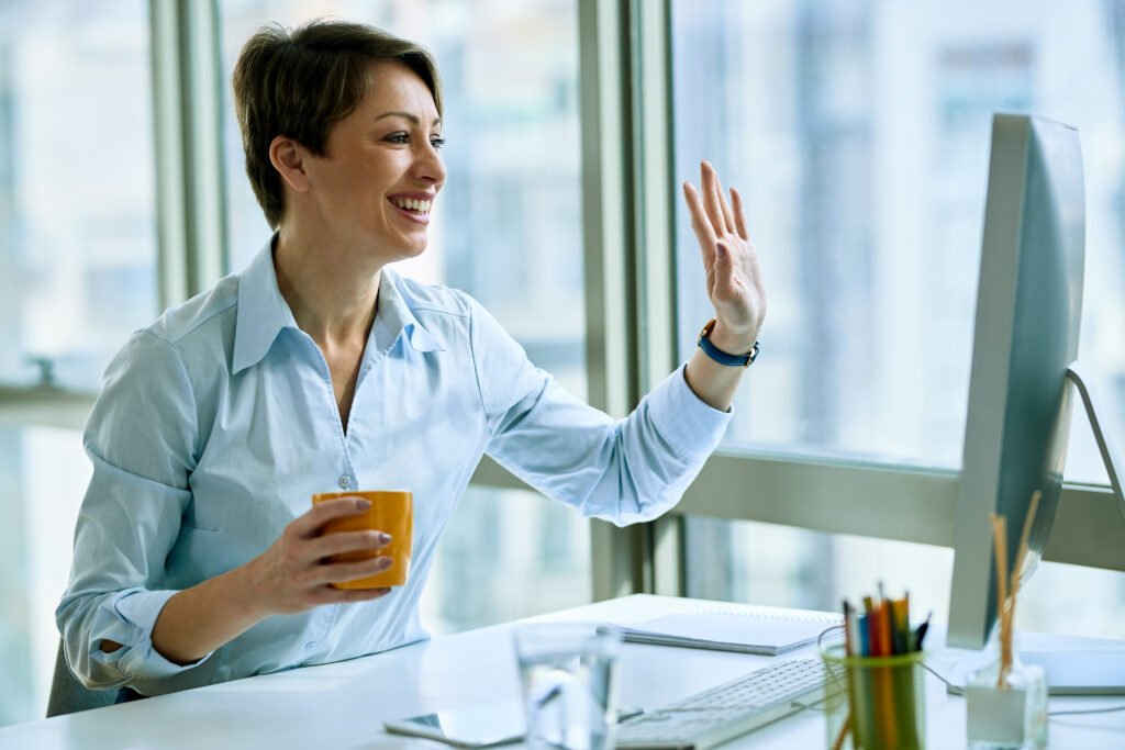Happy businesswoman waving while using computer and making video
